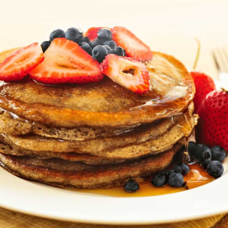 plate of pancakes topped with syrup, blueberries and strawberries